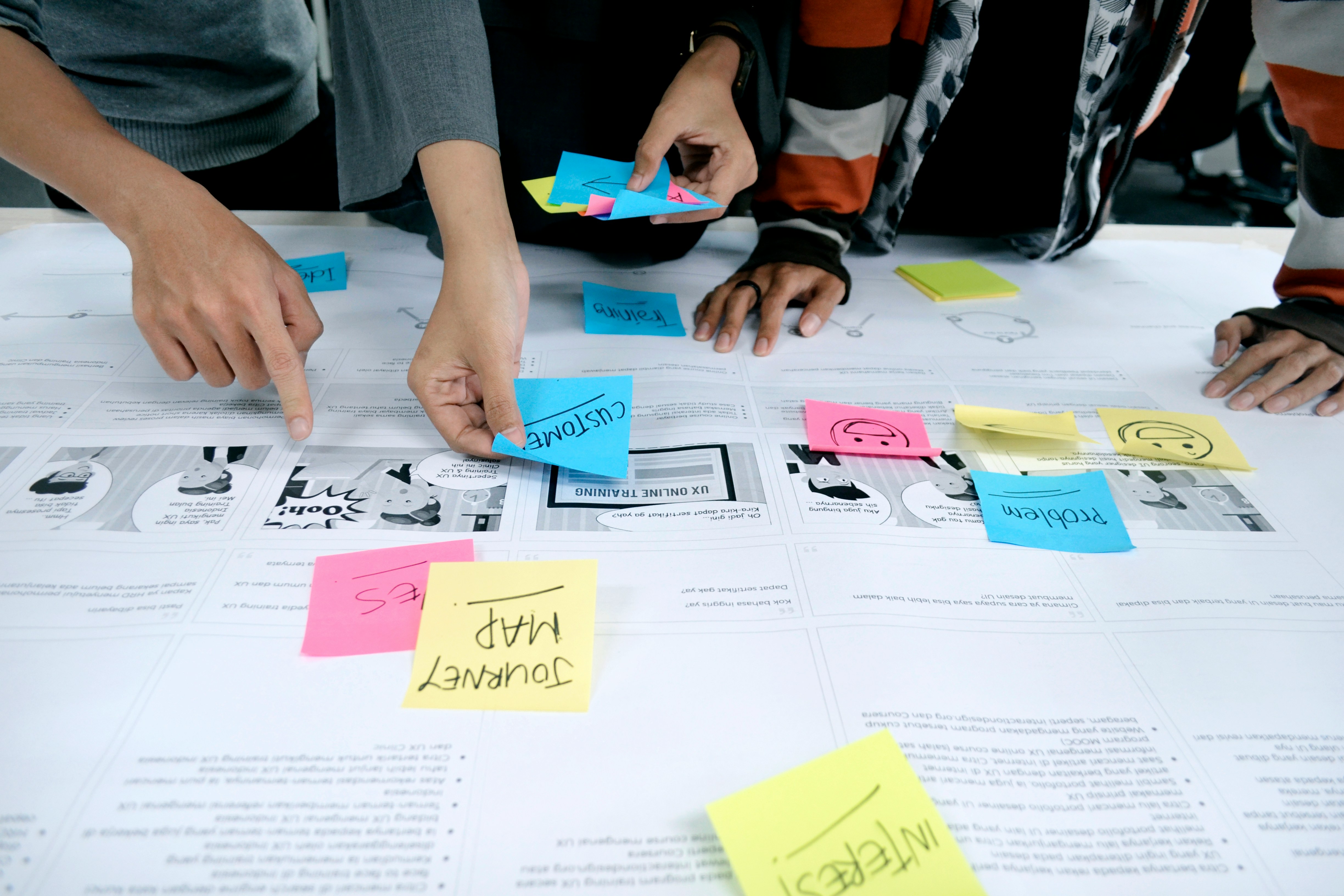 Multiple people placing sticky notes on a table planning and strategizing.