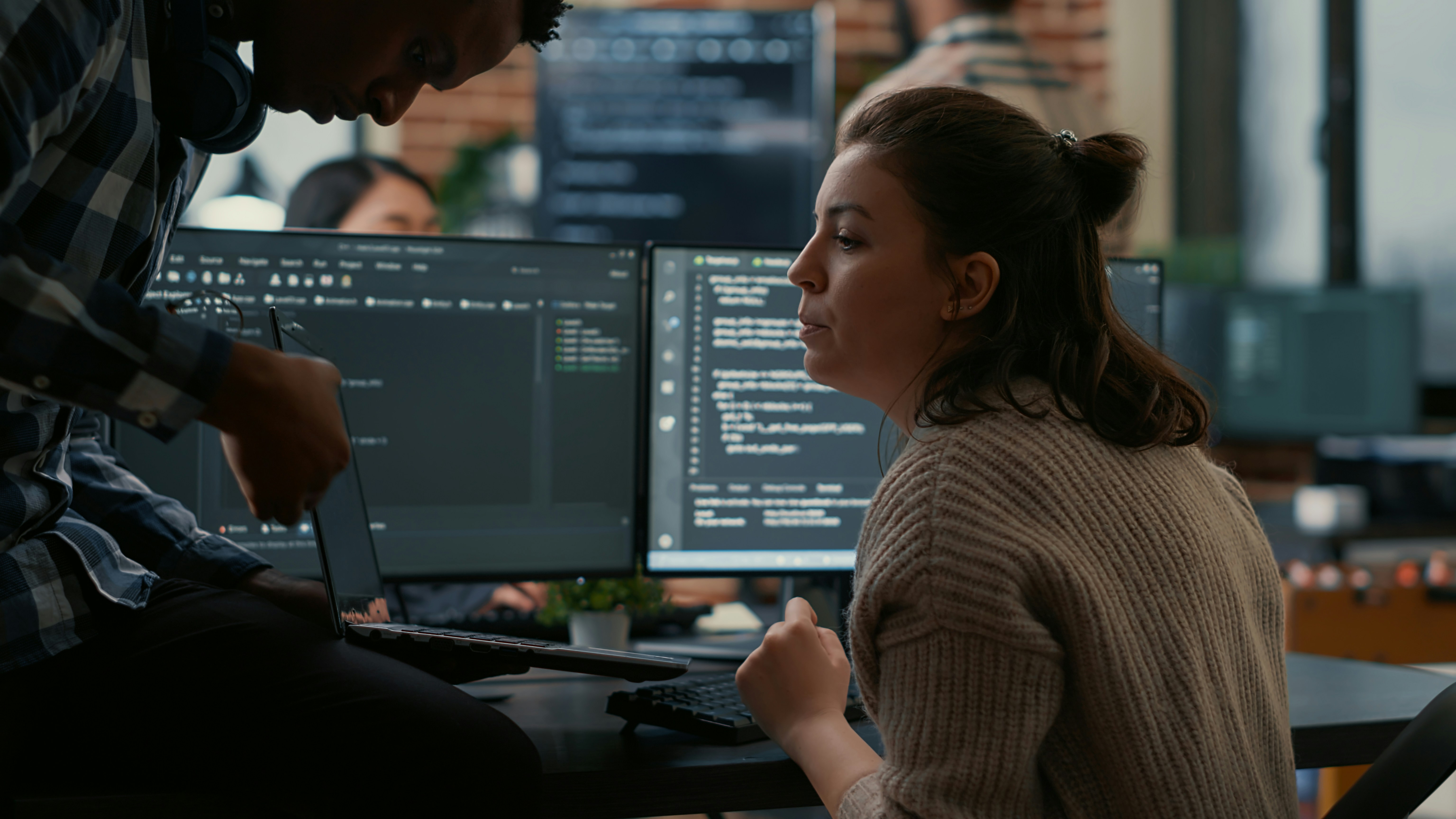 Software consultant pointing to a laptop screen to a woman sitting next to other computer screens