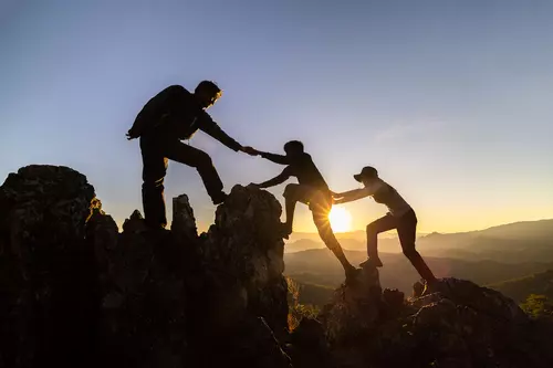 A group of hikers, one helping another up a rock.